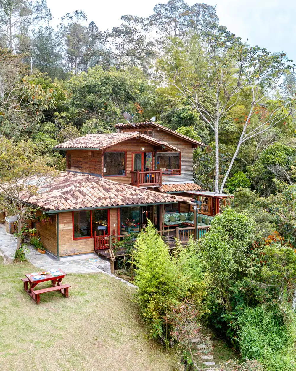 Casa de finca de vereda con techo de teja, entre árboles y jardín.
