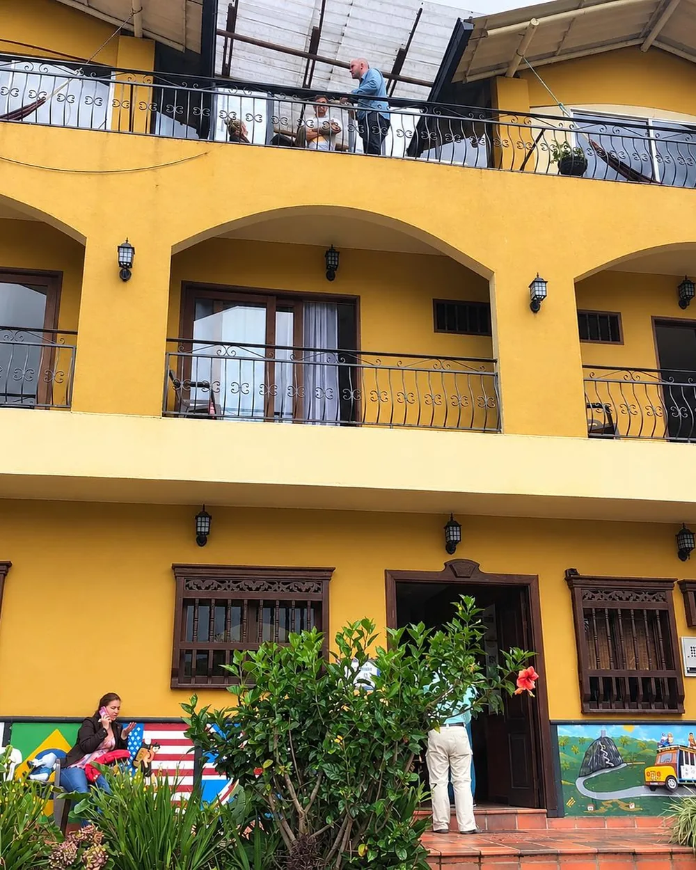 Fachada amarilla de un hostal de Guatapé, con arcos, balcones de hierro y zócalos pintados al pie.