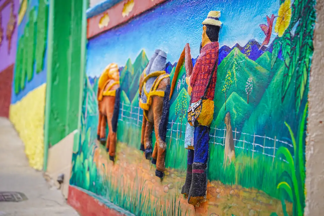 Zócalo en relieve con un arriero y sus mulas cargadas entre montañas verdes.